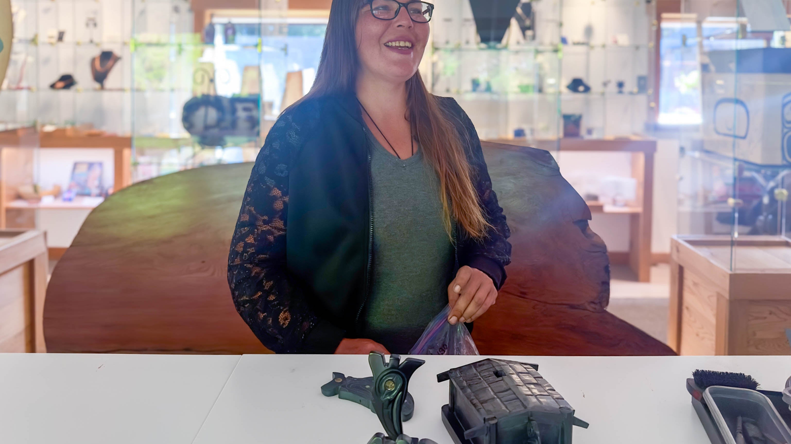 Amy Edgars standing behind a white table with argillite carvings at Crystal Cabin Gallery