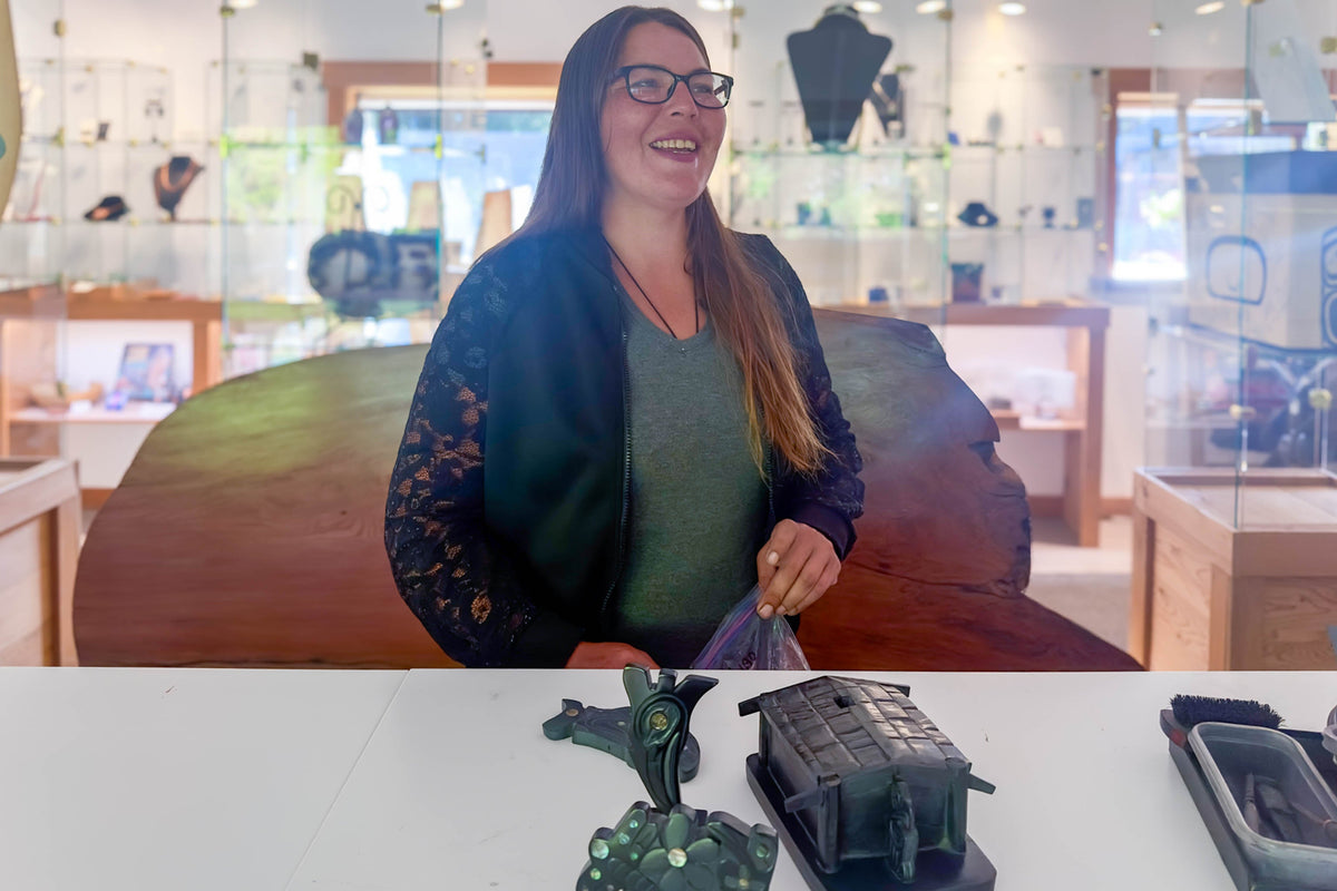 Amy Edgars standing behind a white table with argillite carvings at Crystal Cabin Gallery