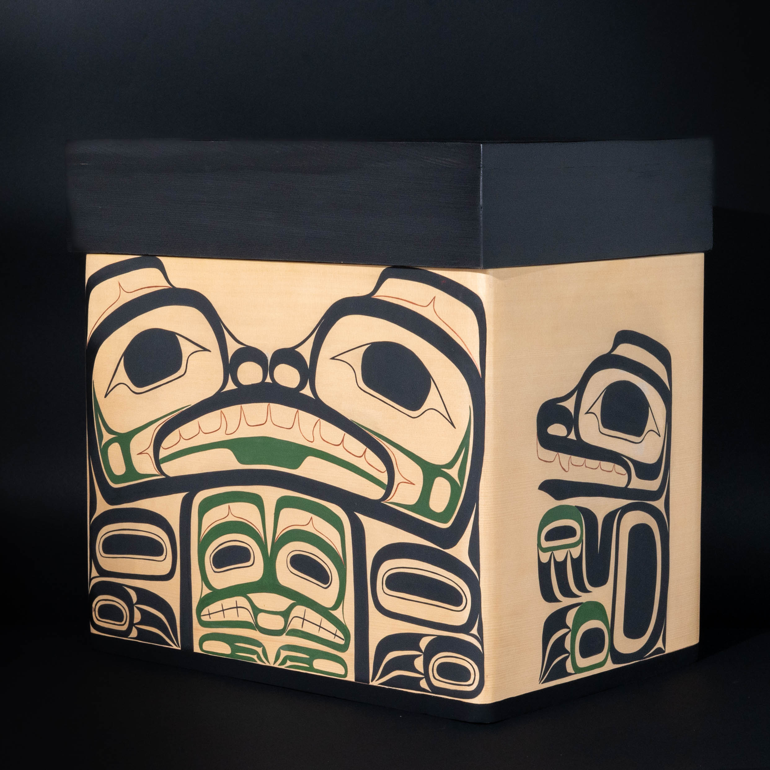 Front of Haida bentwood box showcasing Bear mother in haida formline painting and mouse woman tucked below her, her cub on the right hand side of the box on a black background