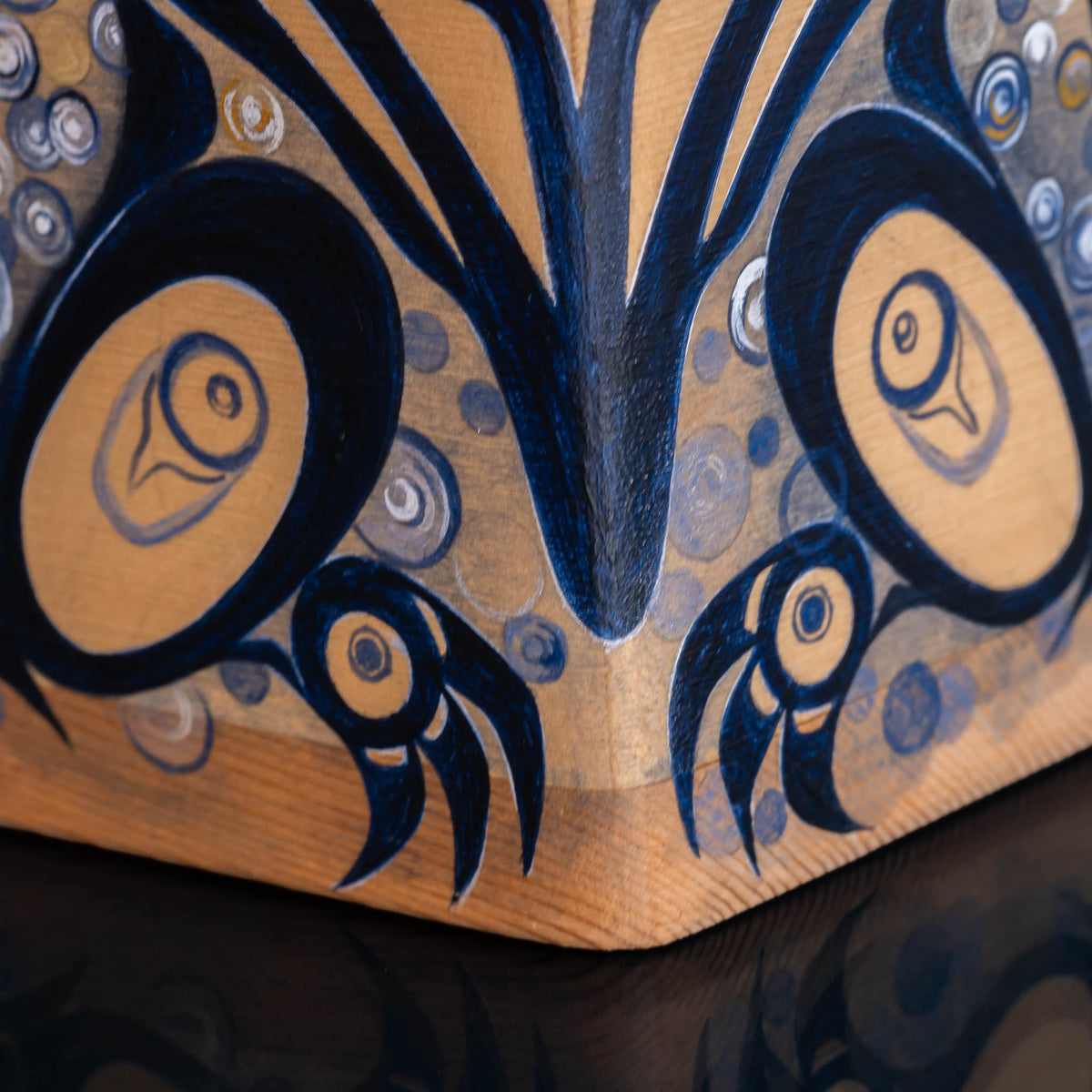 Close-up of a handcrafted wooden box with intricate hand-painted designs in dark blue and natural wood tones.
