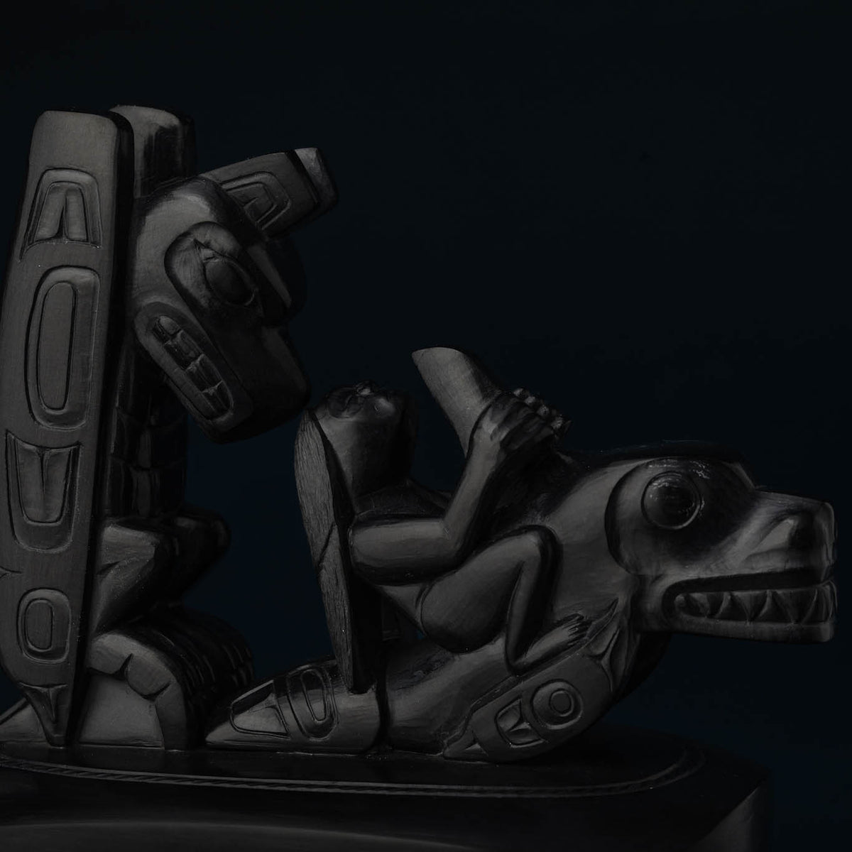 Close-up of a black stone carving with a thunderbird and human figure on top of an orca.