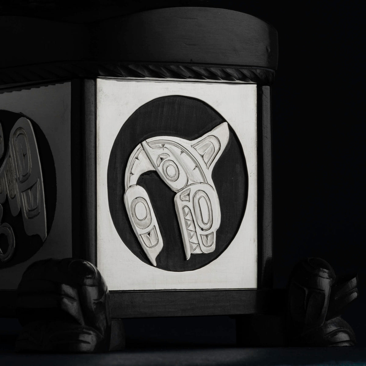 Silver formline killer whale carving inset in blackstone on a dark background.
