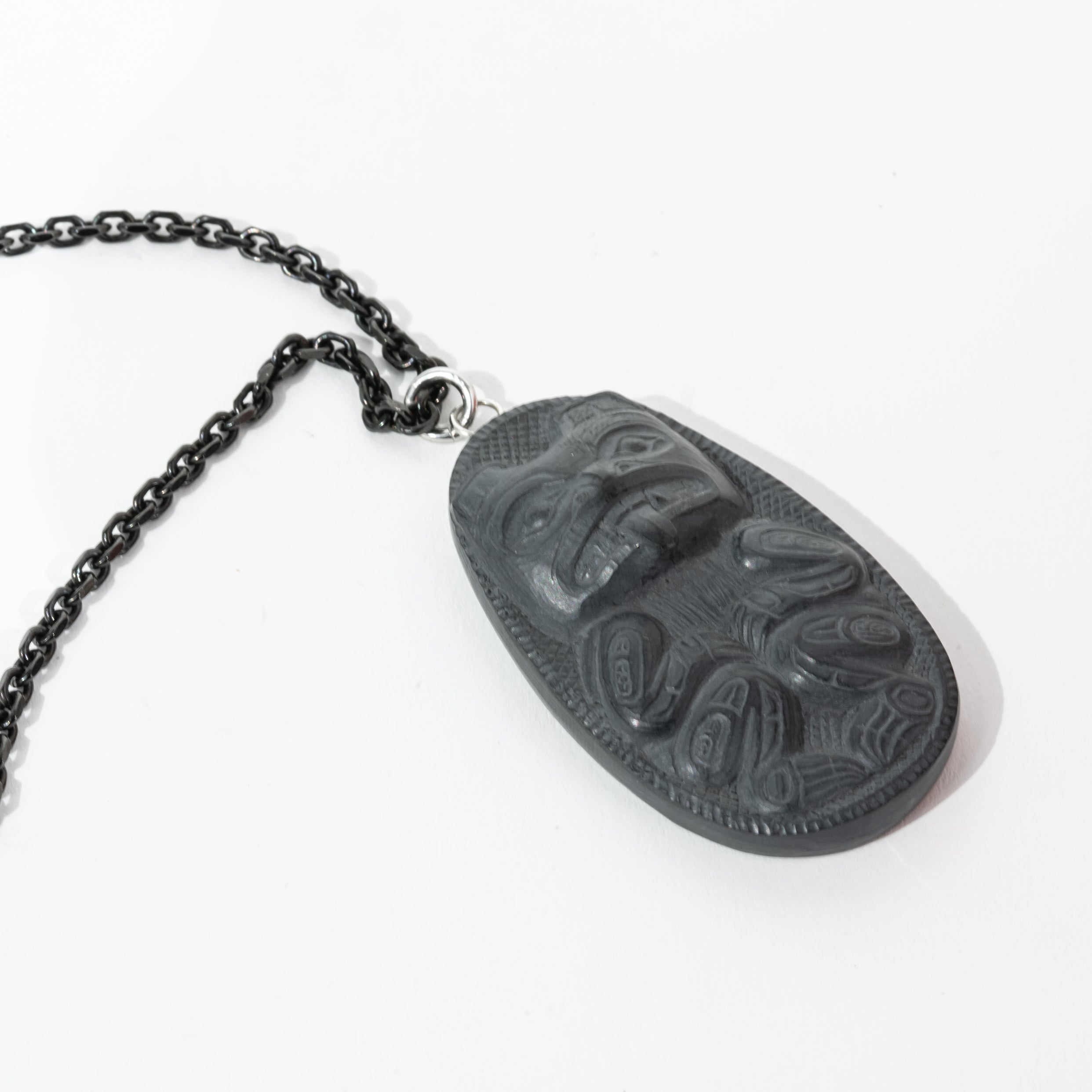 Close up of left side of Black Argillite Bear pendant necklace with intricate Haida Carvings showcasing the 3-d depth of the carving on a white background made by Local Haida Gwaii Artist Melanie Russ