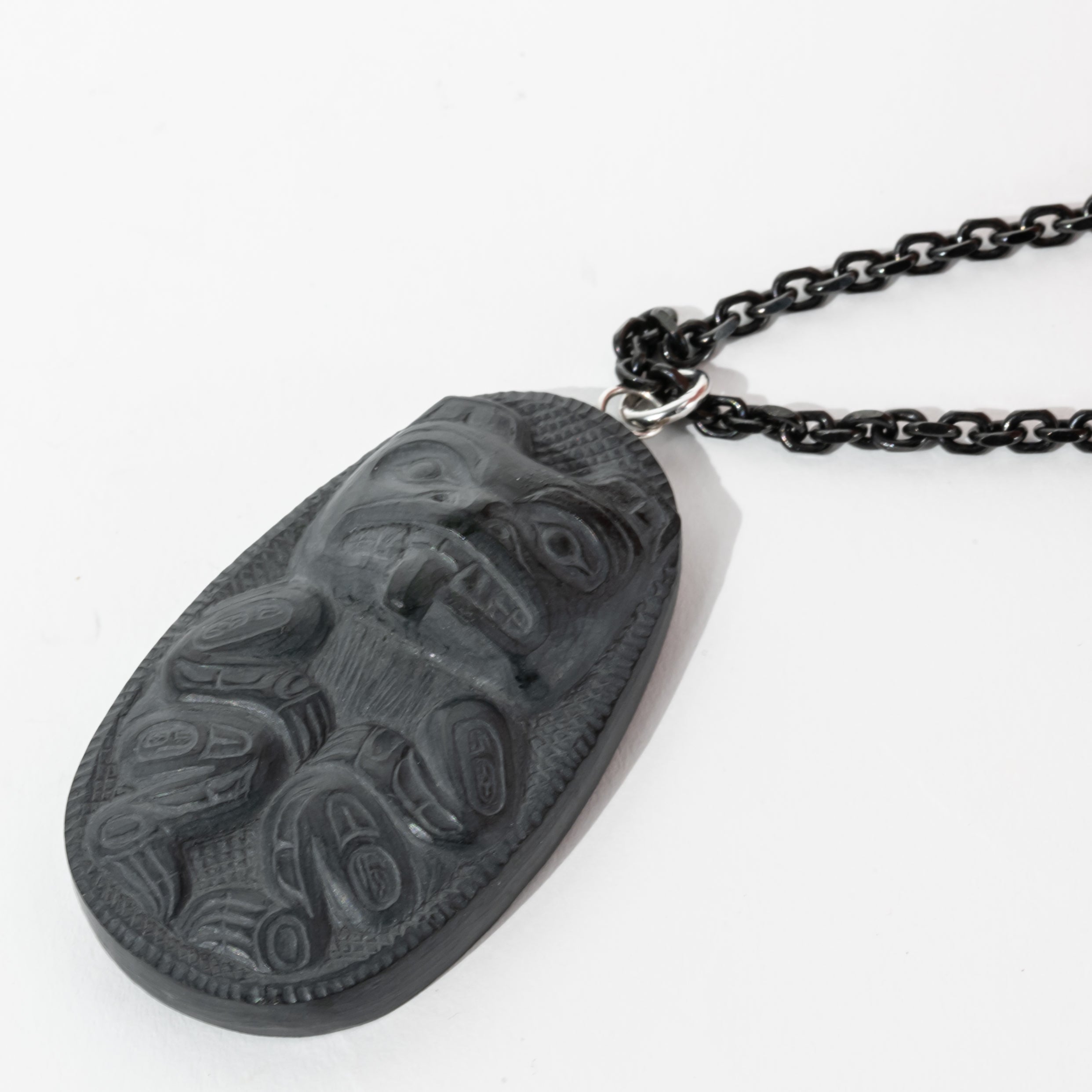 Close up of right side of Black Argillite Bear pendant necklace with intricate Haida Carvings showcasing the 3-d depth of the carving on a white background made by Local Haida Gwaii Artist Melanie Russ