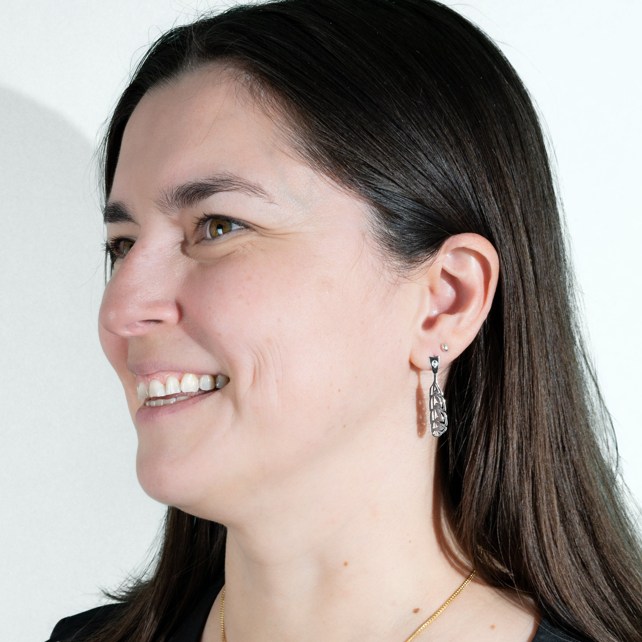 Life style photo of model wearing sterling silver gina mae manifesto feather earrings smiling and looking of into the distance