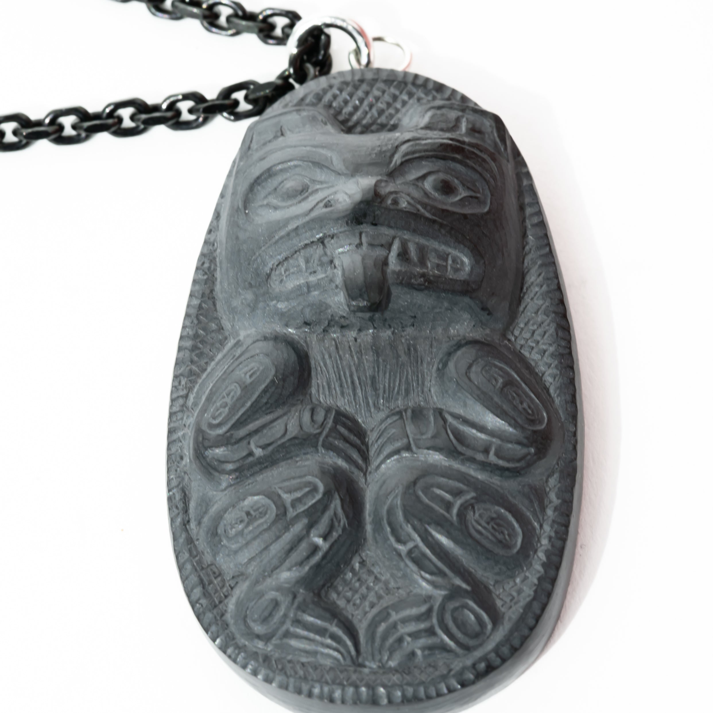 Close up of right side of Black Argillite Bear pendant necklace with intricate Haida Carvings showcasing the 3-d depth of the carving on a white background made by Local Haida Gwaii Artist Melanie Russ