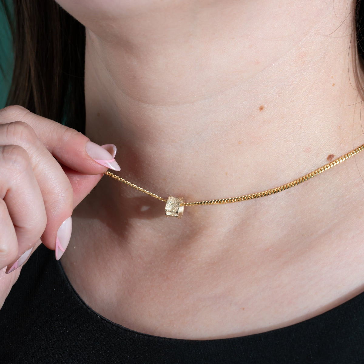 Gold necklace with a small salmon bone vertebrae pendant being adjusted on a person's neck against a green background