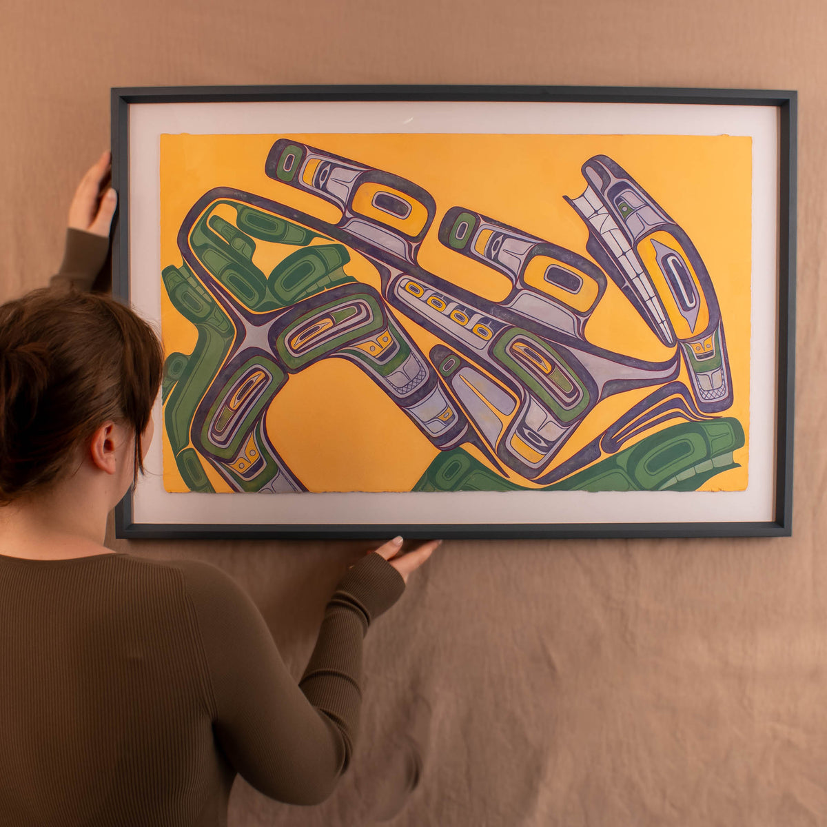 Person holding a framed abstract artwork with geometric shapes on a yellow background