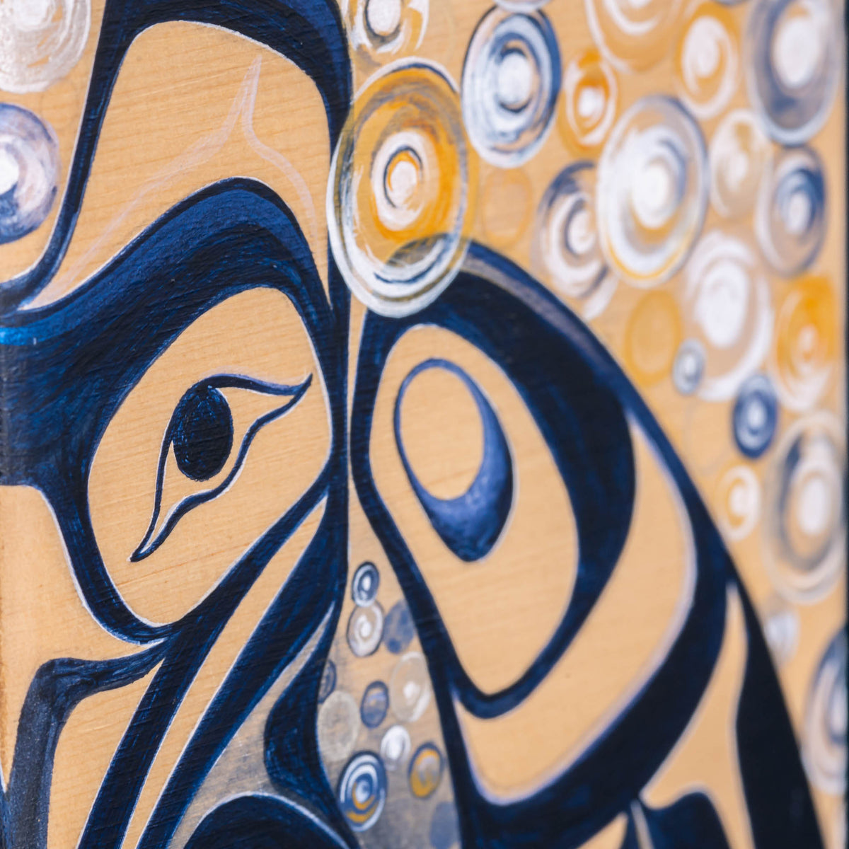 Close-up of a painted abstract artwork featuring a stylized bird in deep navy blue on a warm tan background, with layered circular and oval forms in white, blue, and yellow.