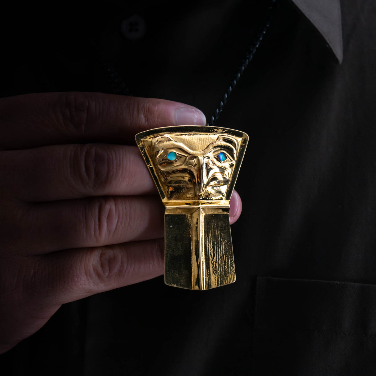 A male model holds a gold shield pendant with an eagle design and blue eyes