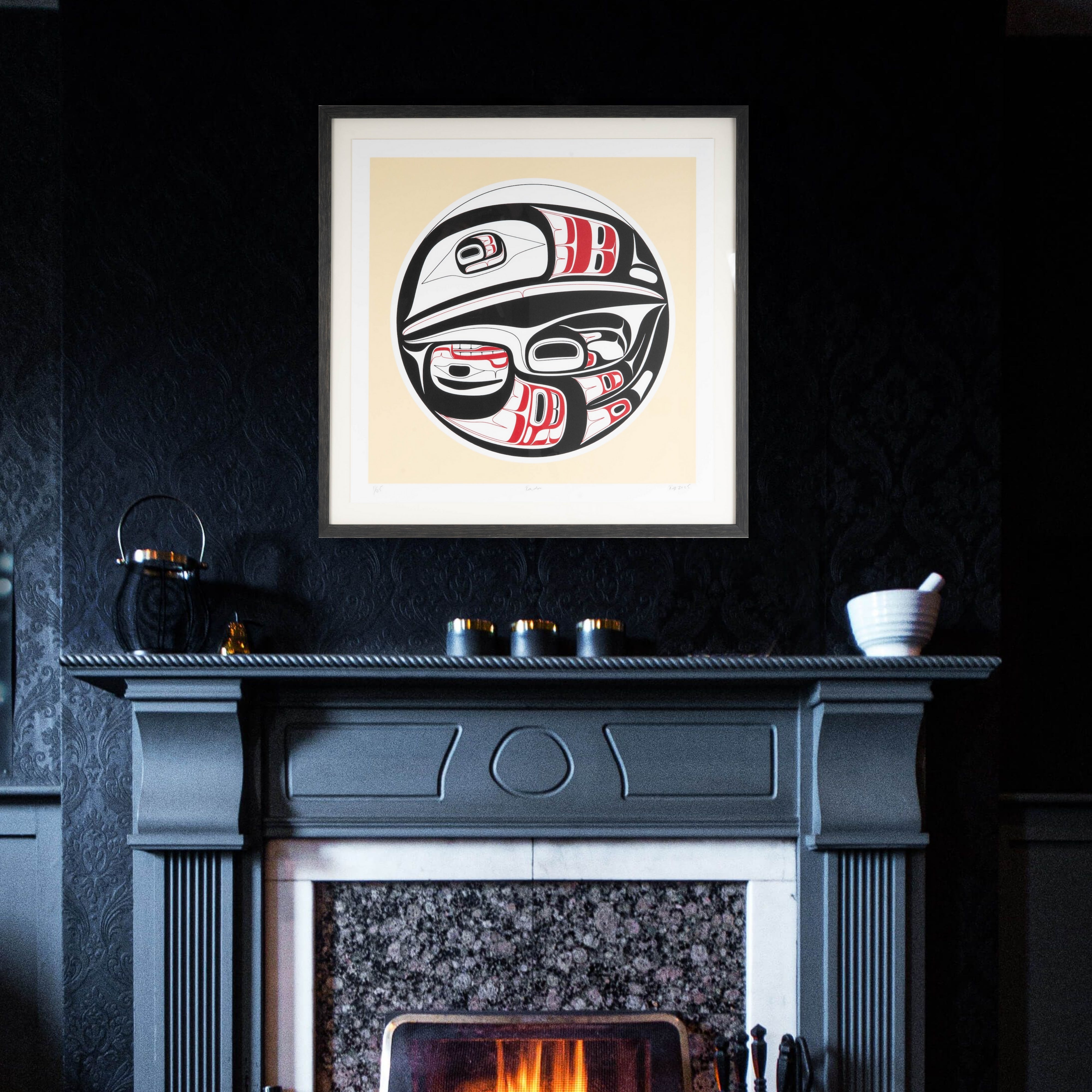 Framed artwork of formline Raven above a fireplace with a dark wall background