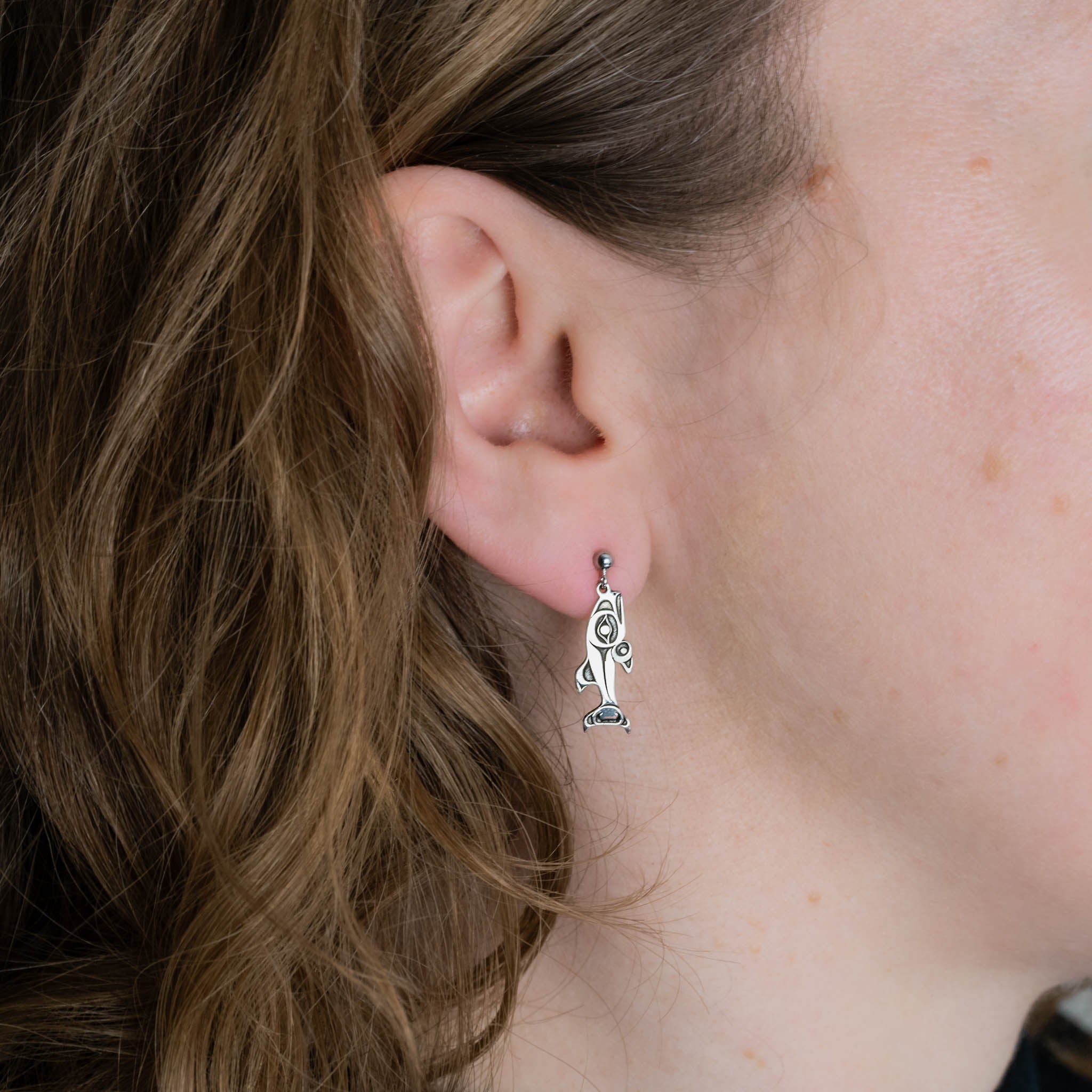 Close-up of a person wearing a silver salmon stud earring.