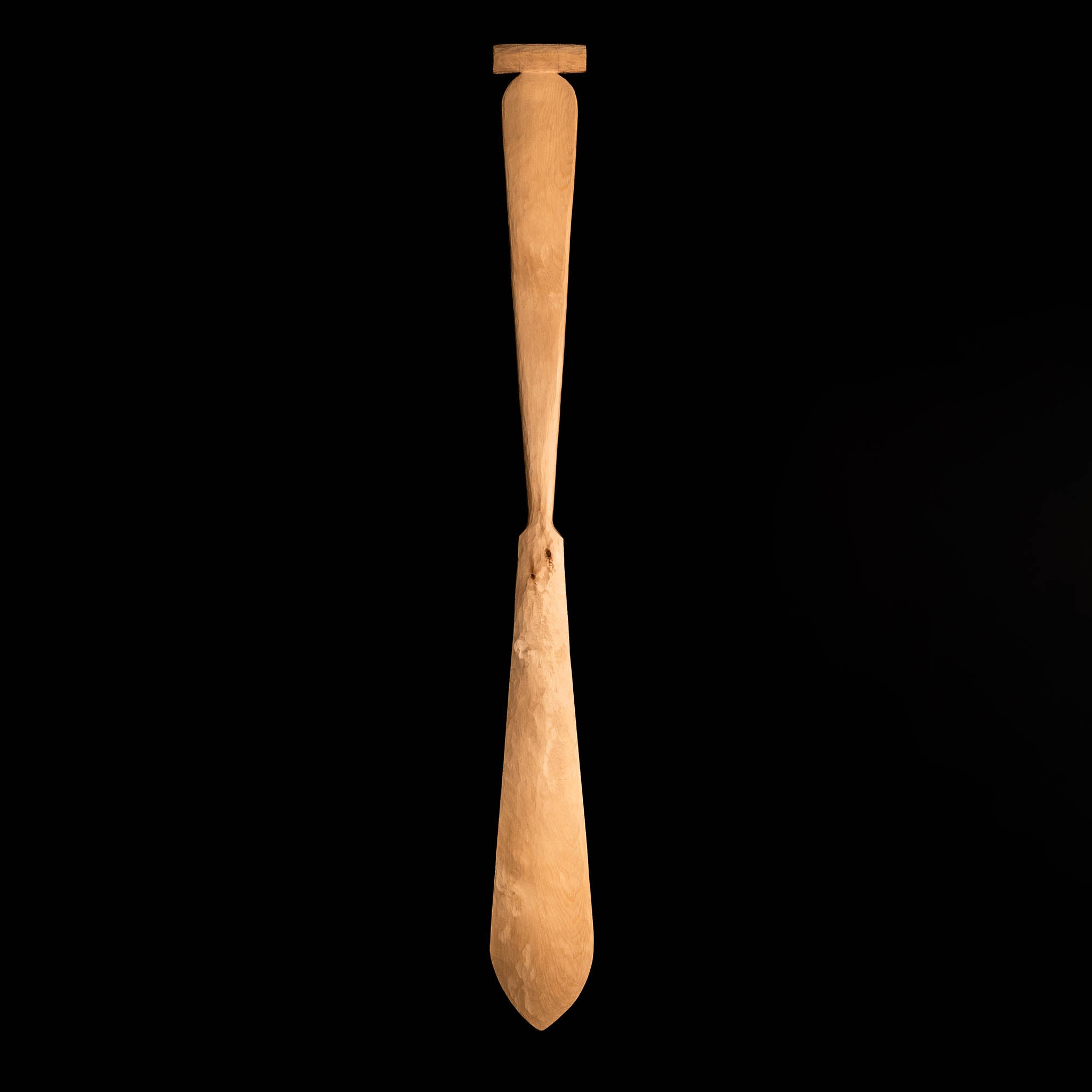 Hand carved wooden paddle on a black background.