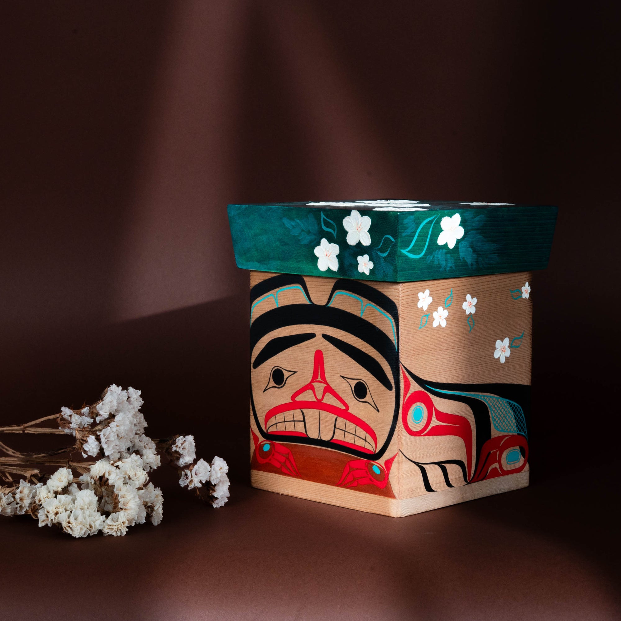Haida Bentwood box with a stylized formline beaver face design featuring red, black, and blue colours on a dark background.