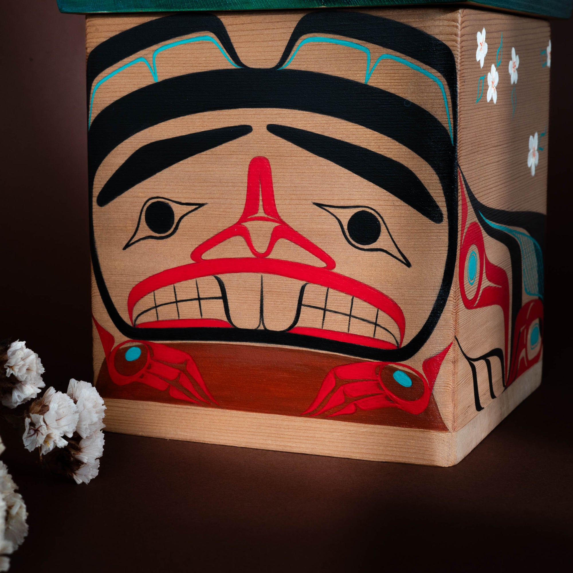 Haida Bentwood box with a stylized formline beaver face design featuring red, black, and blue colours on a dark background.