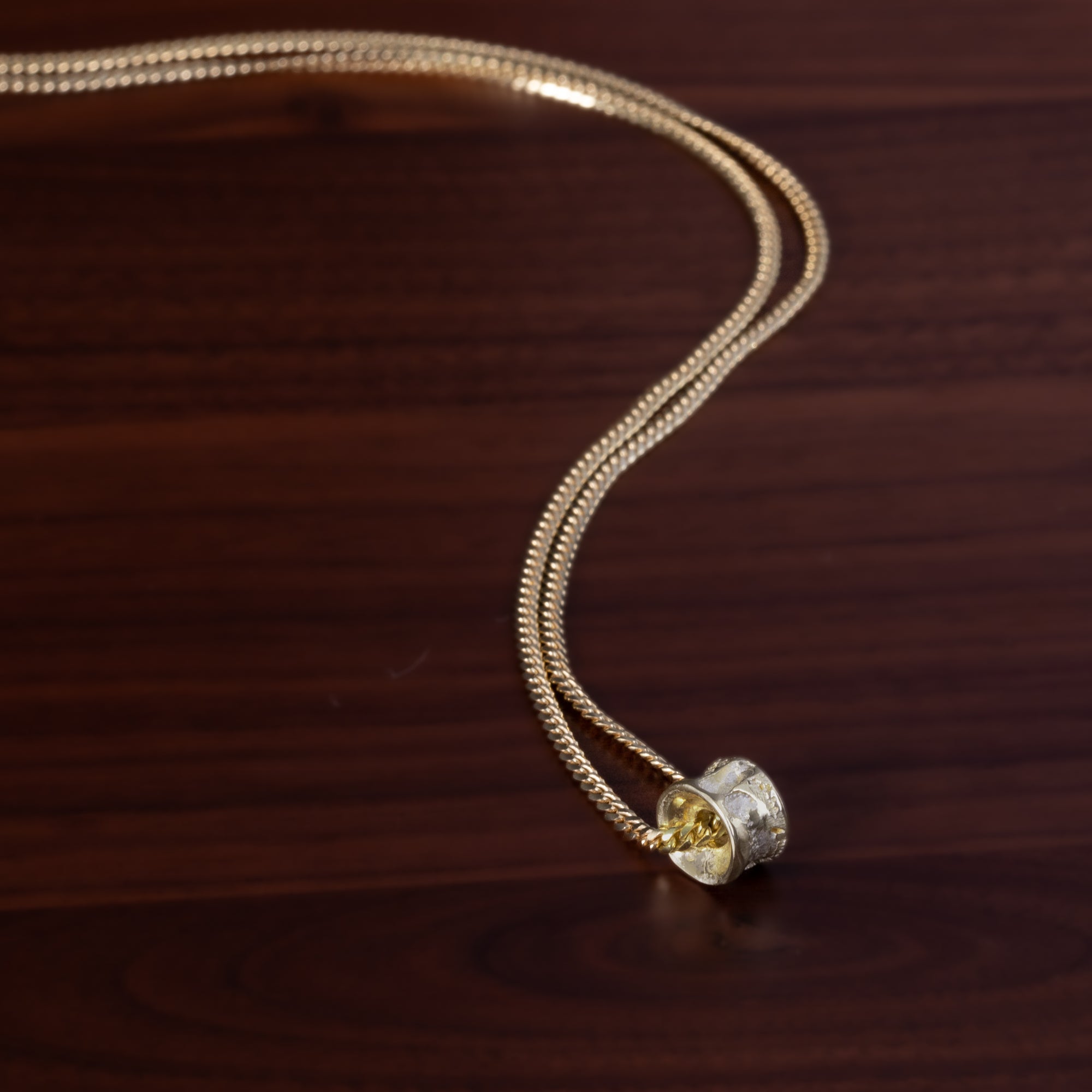 Gold salmon bone vertebrae on a gold chain by ts'mysen artist morgan asoyuf on a dark wooden surface