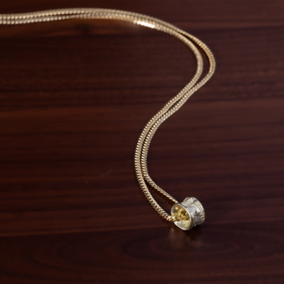 Gold salmon bone vertebrae on a gold chain by ts'mysen artist morgan asoyuf on a dark wooden surface