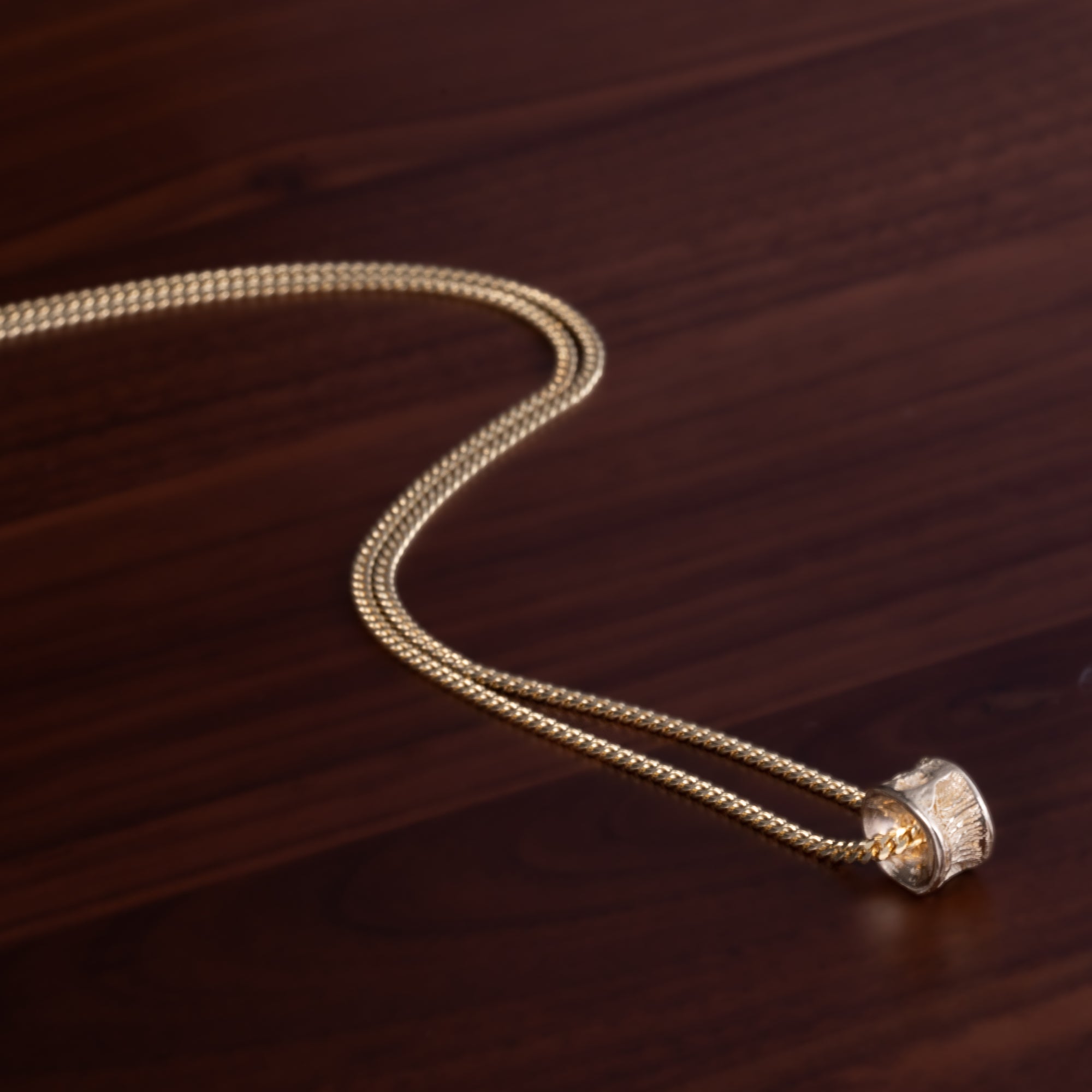 Close up of Gold salmon bone vertebrae on a gold chain by ts'mysen artist morgan asoyuf on a dark wooden surface