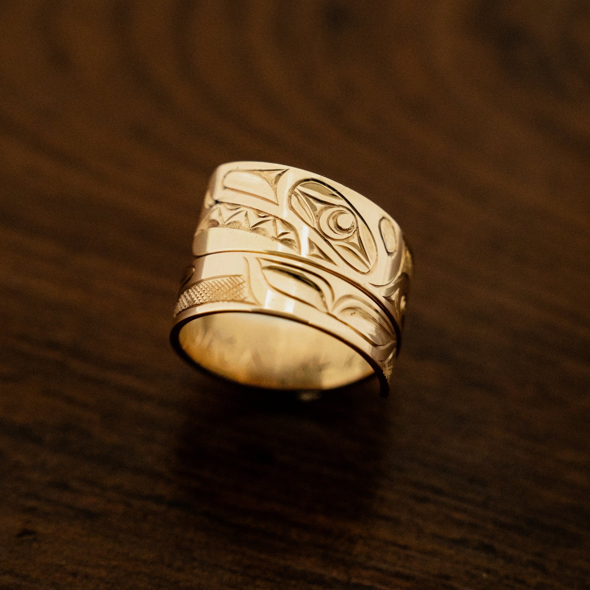 Closeup of gold engraved wrap ring with a brown wood background