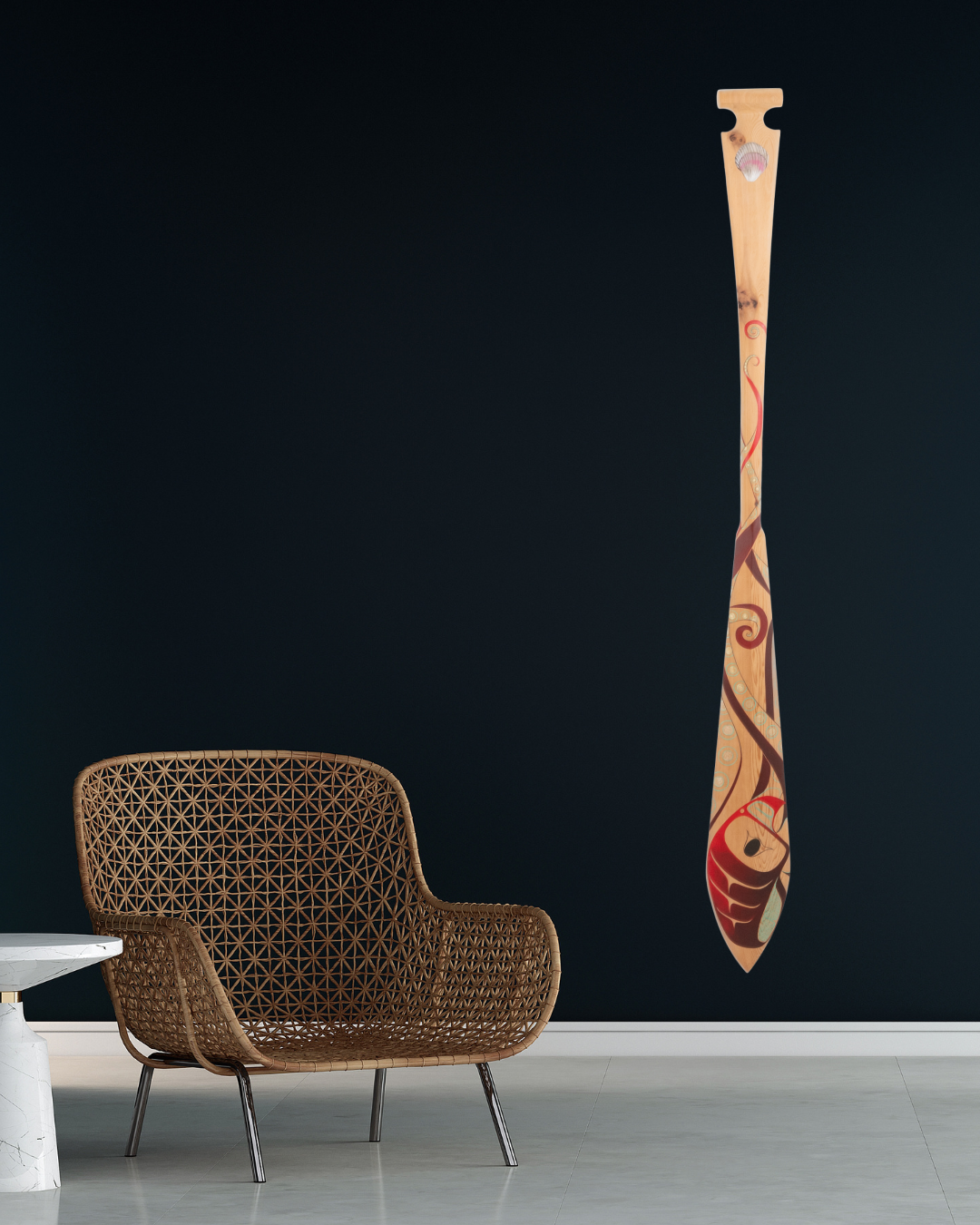 Wooden paddle with decorative design hanging on a black wall next to a wicker chair.