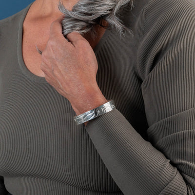 Person wearing a gray ribbed sweater with a Hand carved sterling silver Raven bracelet by Haida artist Alvin Adkins side view on a plain background
