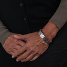 Close-up of a person's hands with Hand carved sterling silver hummingbird bracelet by Haida artist Alvin Adkins front view on a dark background