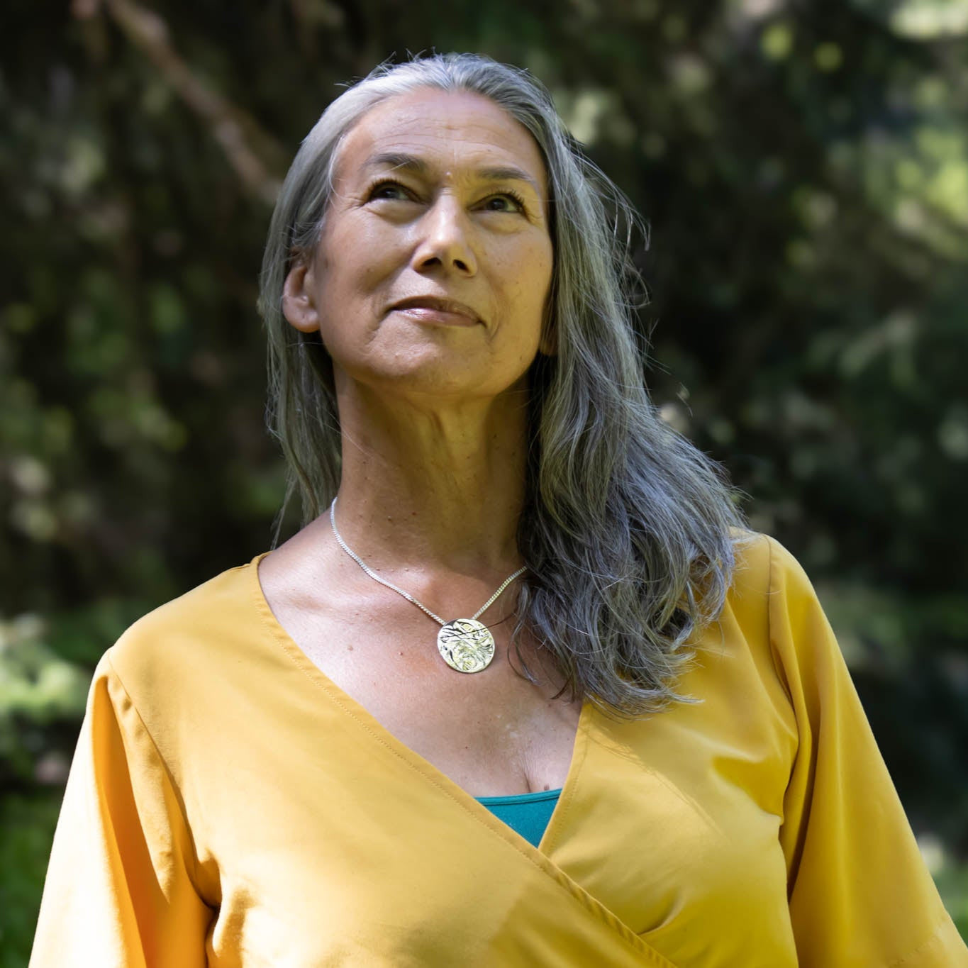 Woman with gray hair wearing a yellow top and Hand carved sliver eagle pendant by the Tlell river
