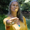 Woman holding a yellow flower outdoors with greenery in the background