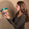 Woman holding a Haida Bentwood box with a colourful formline Beaver and floral formline design against a plain background