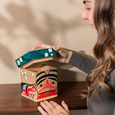 Person opening a wooden box with artistic design on a wooden surface