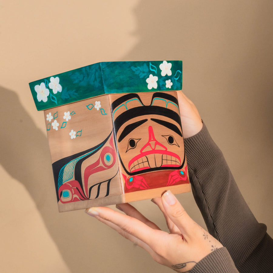  Hand holding a Haida Bentwood box with a colourful formline Beaver and floral formline design against a plain background