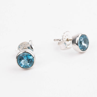 Silver earrings with blue gemstones on a white background with one earring facing forward and one earring facing to the side