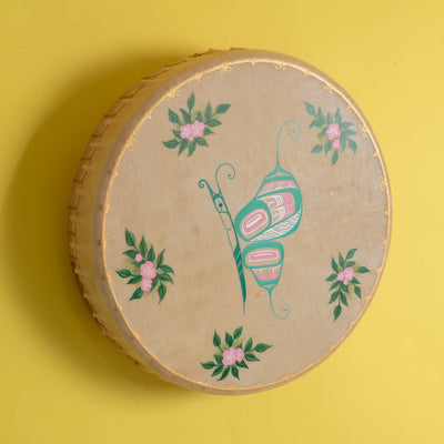 Tan drum with colourful shimmering butterfly in the center and flowers with a painted gold frame, on a yellow background.