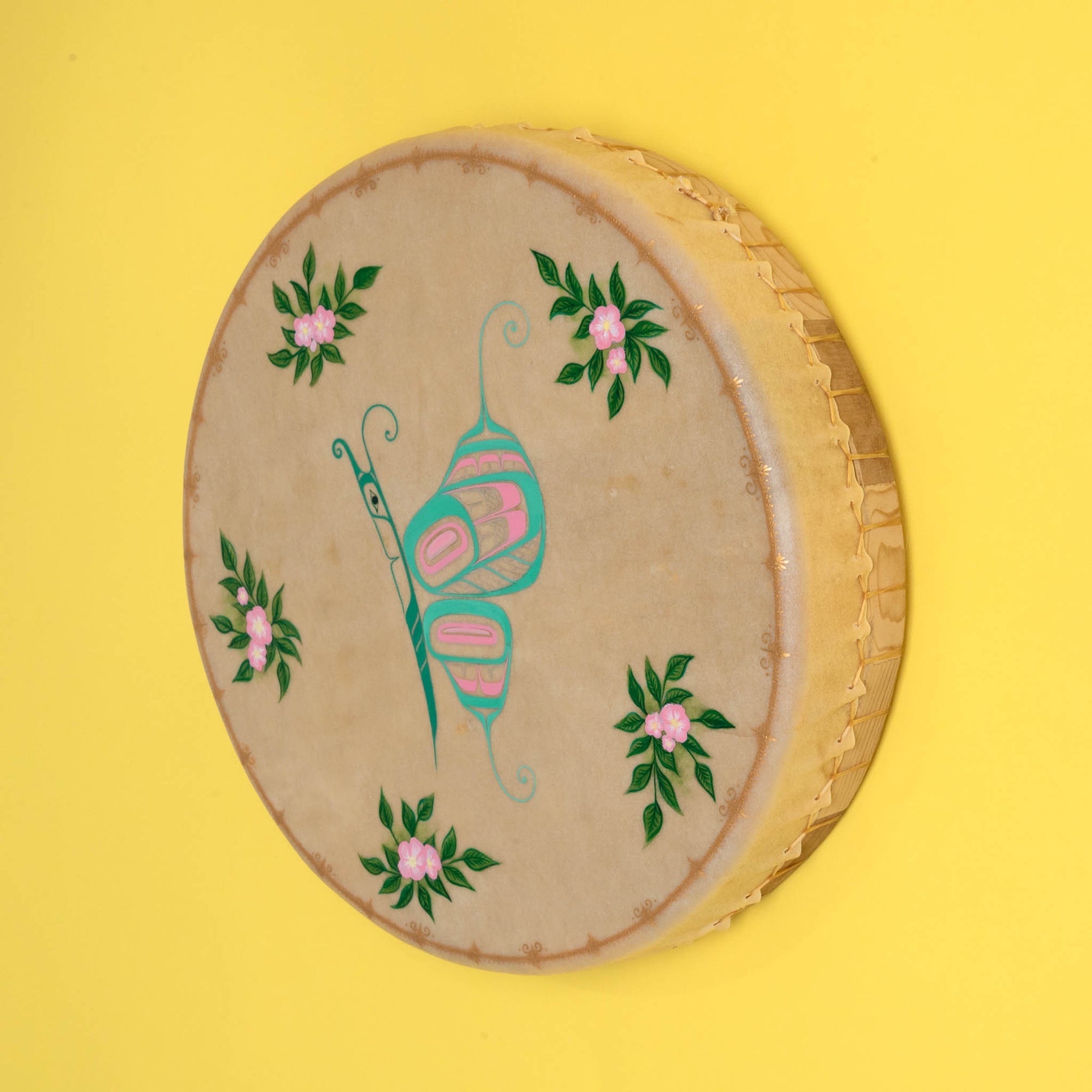 Tan drum with colourful butterfly in the center and flowers with a pinted gold frame, on a yellow background.