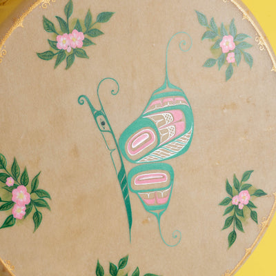 Painted butterfly with shimmering highlights and pink flowers with green leaves on a tan hide with yellow wall.