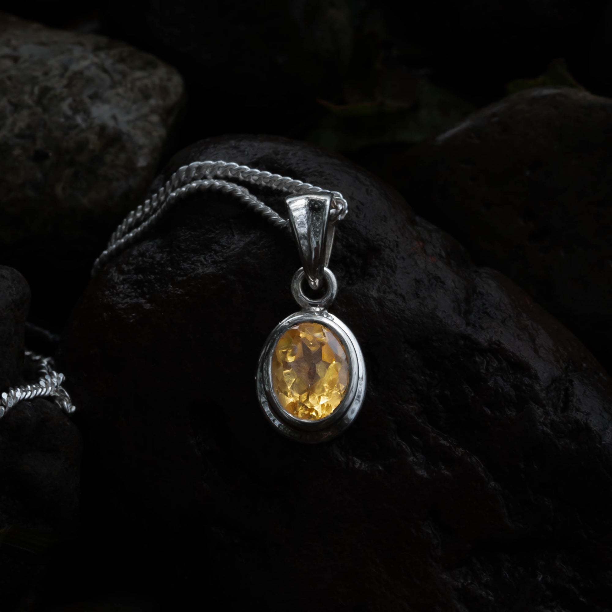 Silver pendant with a yellow gemstone on a dark textured background