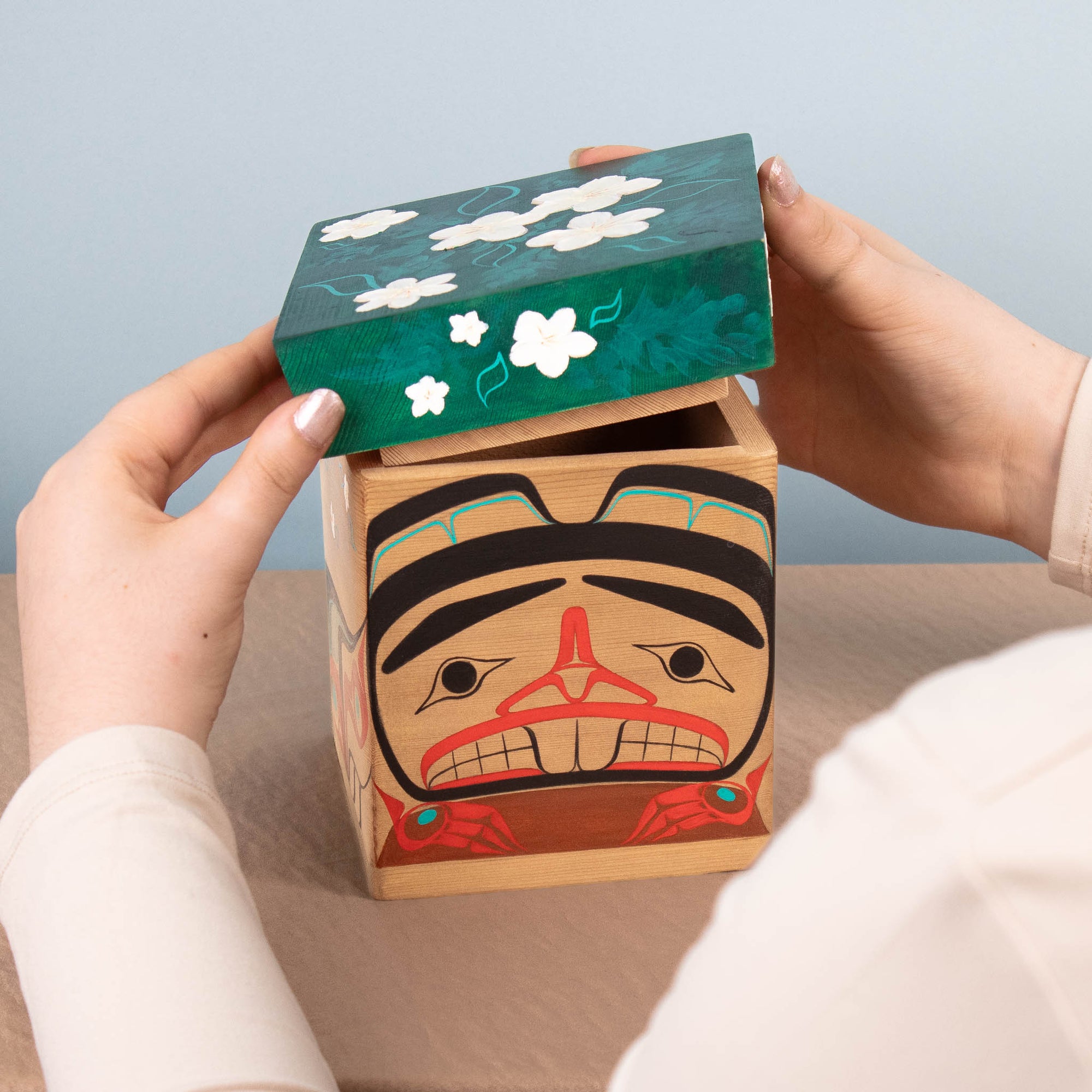 Wooden box with artistic design on lid held by hands against a light blue background
