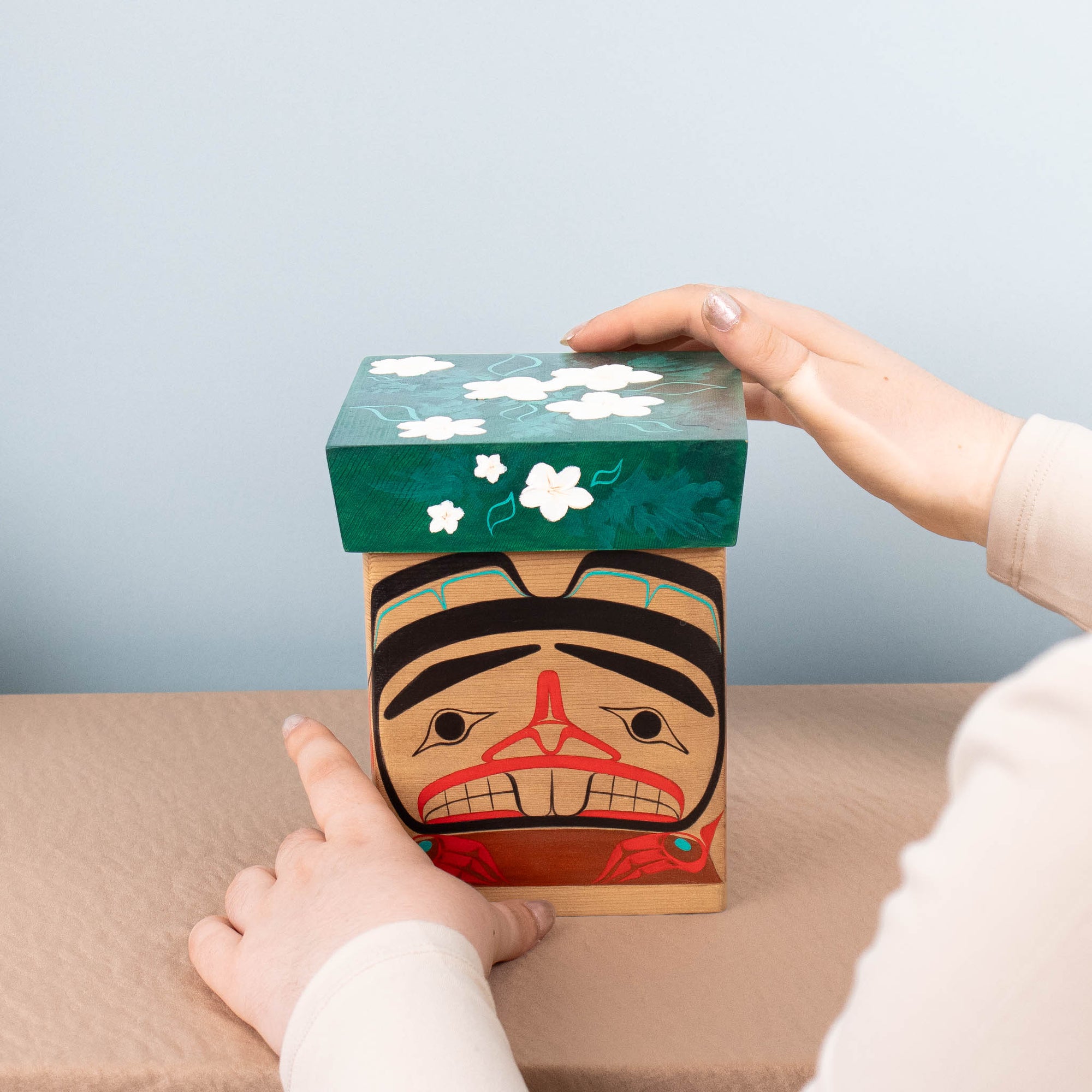 Person holding a decorative box with a face design on a light blue background