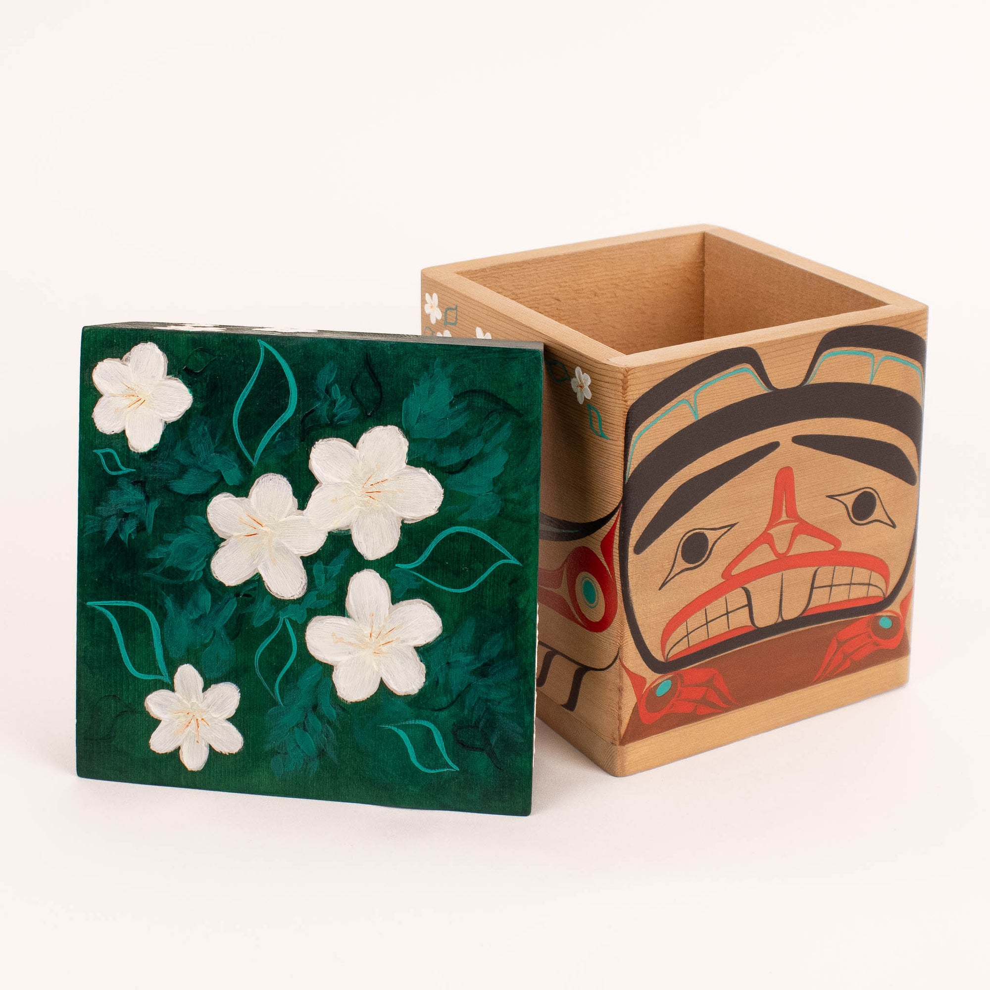 Wooden box with floral design on one side and a face design on the other, on a white background