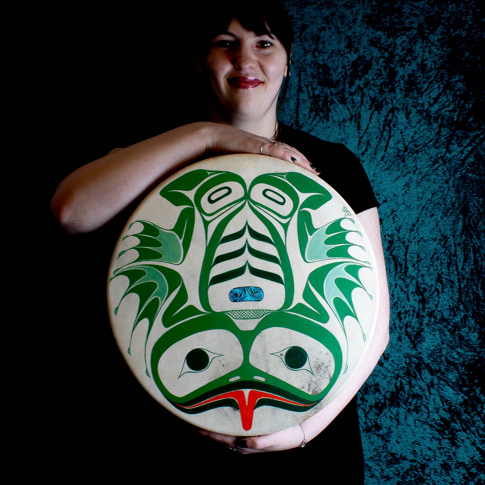Model holding frog drum in formline design with green background