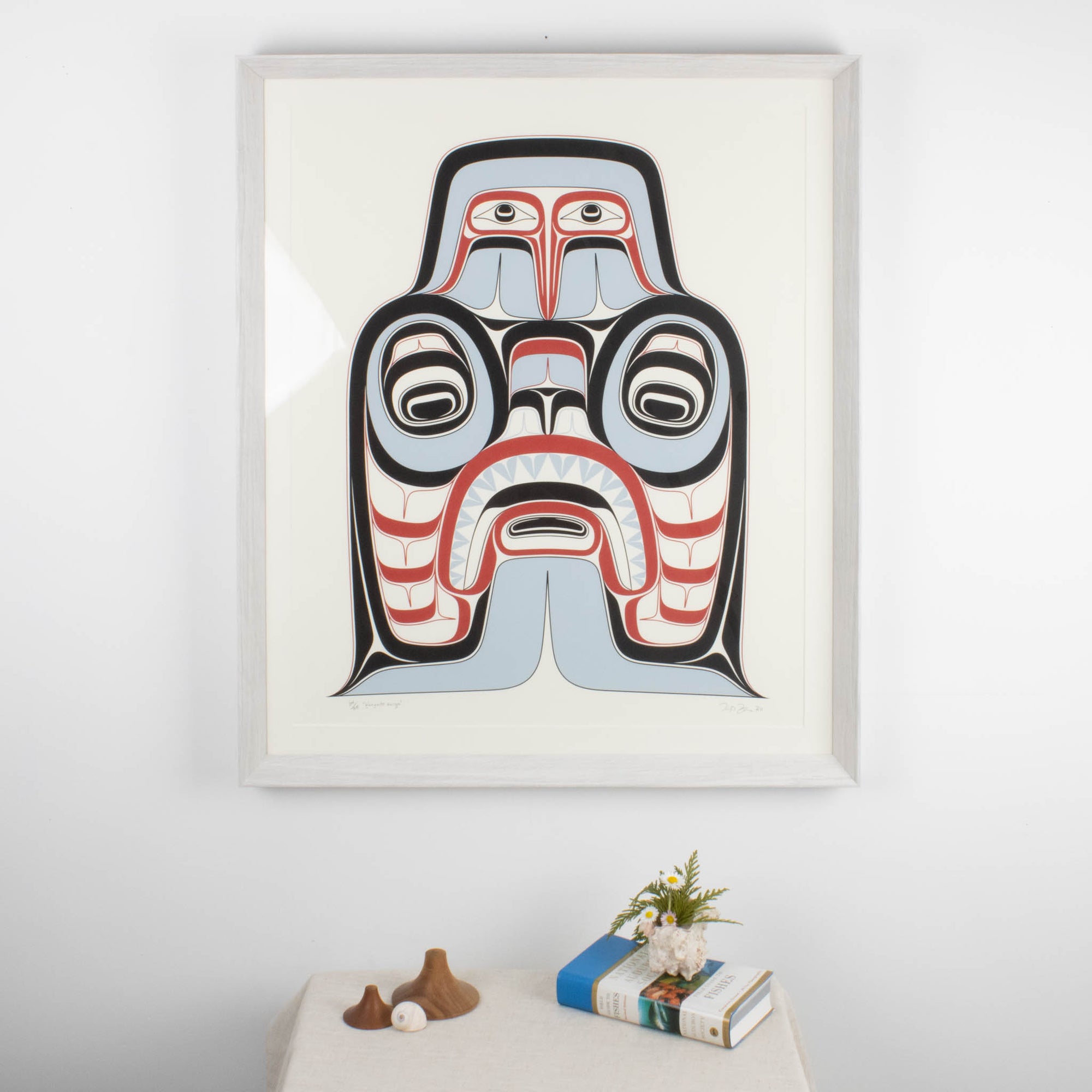 Haida Art print featuring supernatural being Dogfish mother. with bold red and black, and soft blue hues to show contrast, framed in a driftwood was frame. In an interior design.