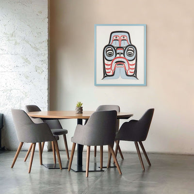 Dining area with a table and chairs, and a framed artwork of Haida Art print featuring supernatural being Dogfish mother. with bold red and black, and soft blue hues to show contrast, framed in a driftwood was frame on the wall.