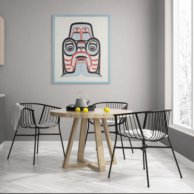 Dining room with a wooden table and black chairs, featuring a colorful abstract painting of  Haida Art print featuring supernatural being Dogfish mother. with bold red and black, and soft blue hues to show contrast, framed in a driftwood was frame on the wall.