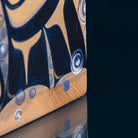 Close-up of a corner of wooden object with hand-painted bubbles in navy blue, beige, and white, showing the wood grain and reflective glass surface.
