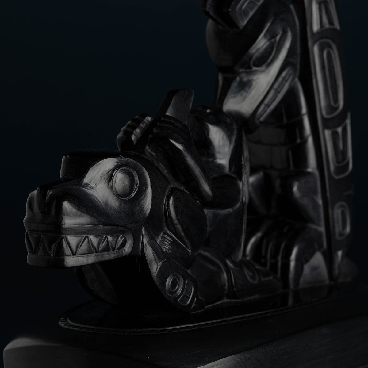 A black stone carving of a killer whale with other creatures fading into the background. 