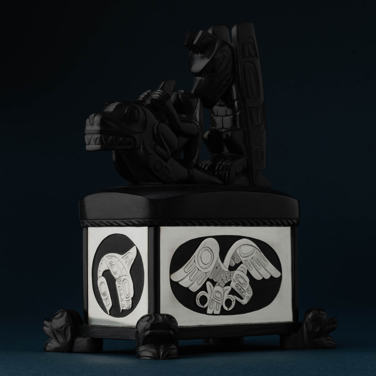An ornately carved box of black material and sterling silver on a dark blue background.