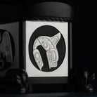 Silver formline killer whale carving inset in blackstone on a dark background.