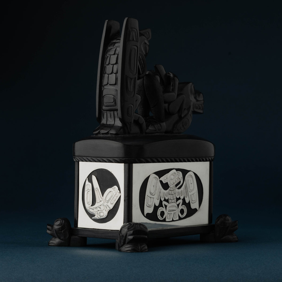 An artistic box showing the back of an animal with feathers and an orca and bird carved into the sterling silver.