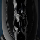 human face carved in black stone holing an object in their hands with rope like carvings on the black stone below.