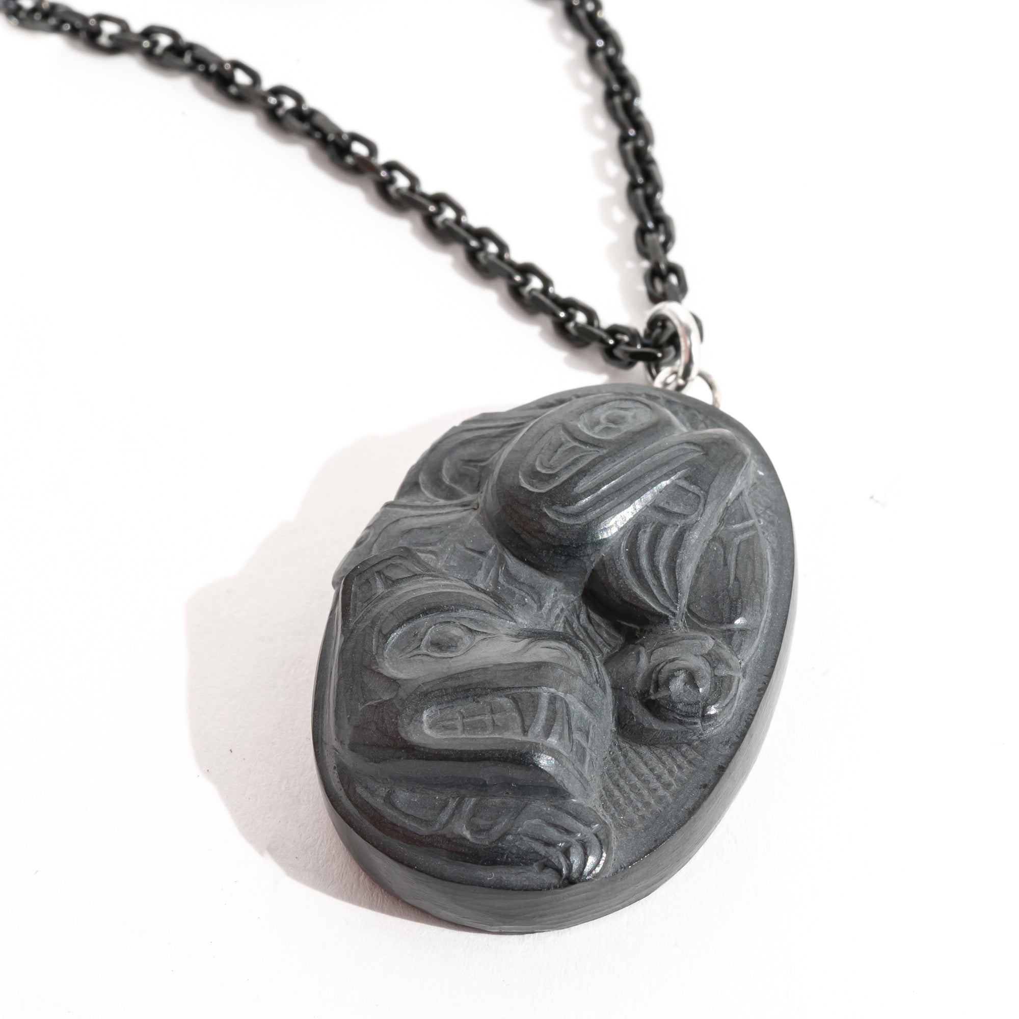 Close up of Black Argillite Sea Bear pendant necklace with intricate Haida Carvings on a white background made by Local Haida Gwaii Artist Melanie Russ